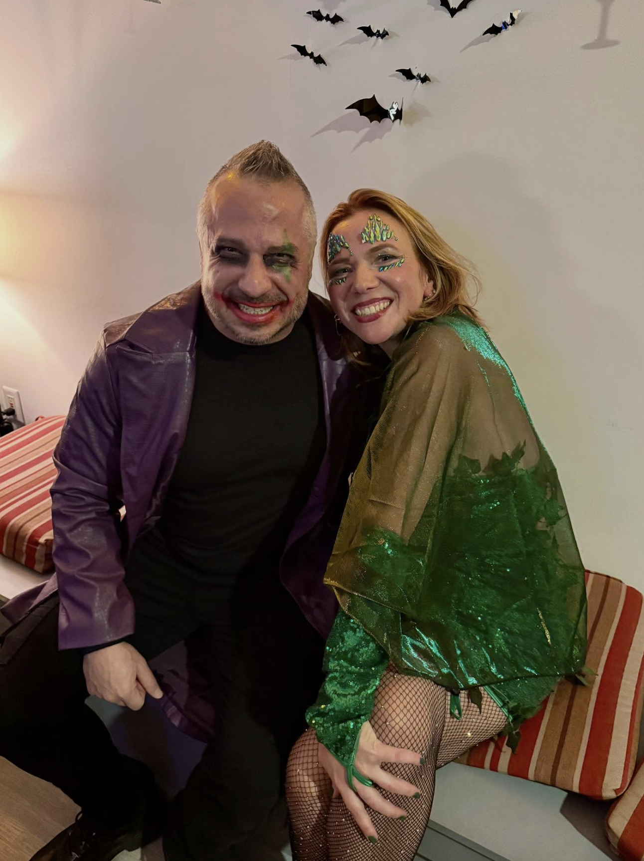 Costumed couple in purple and green outfits posing on the lounge bench