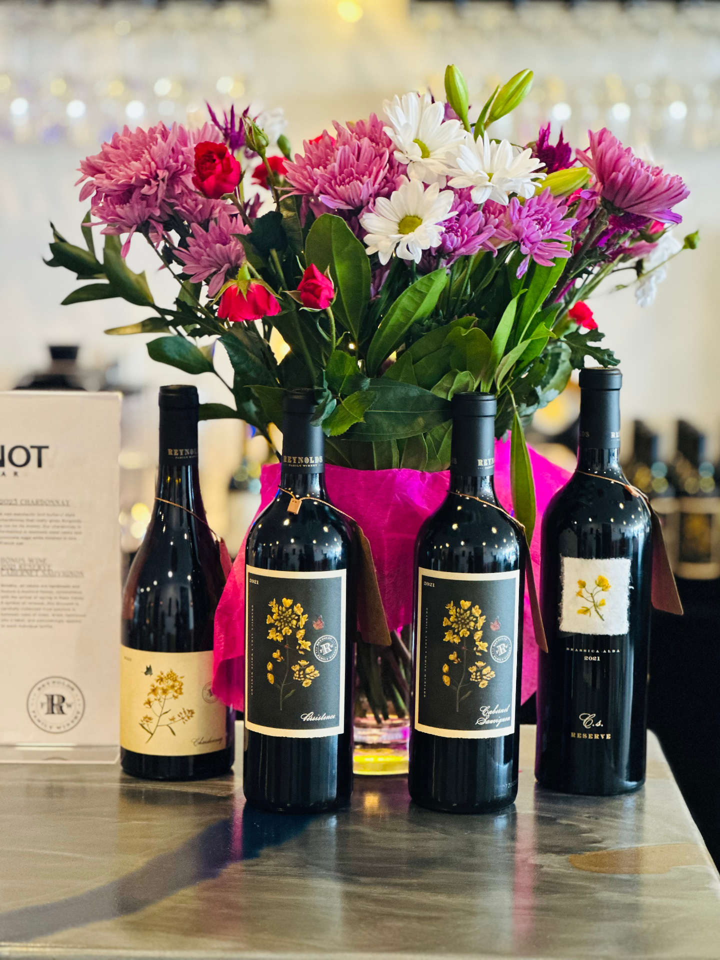 Reynolds Family Winery bottles lined up at the bar in front of a bouquet of pink and white flowers