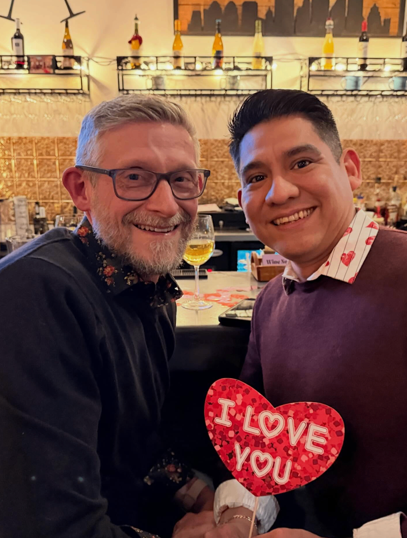 Two friends at the bar holding an I Love You heart sign