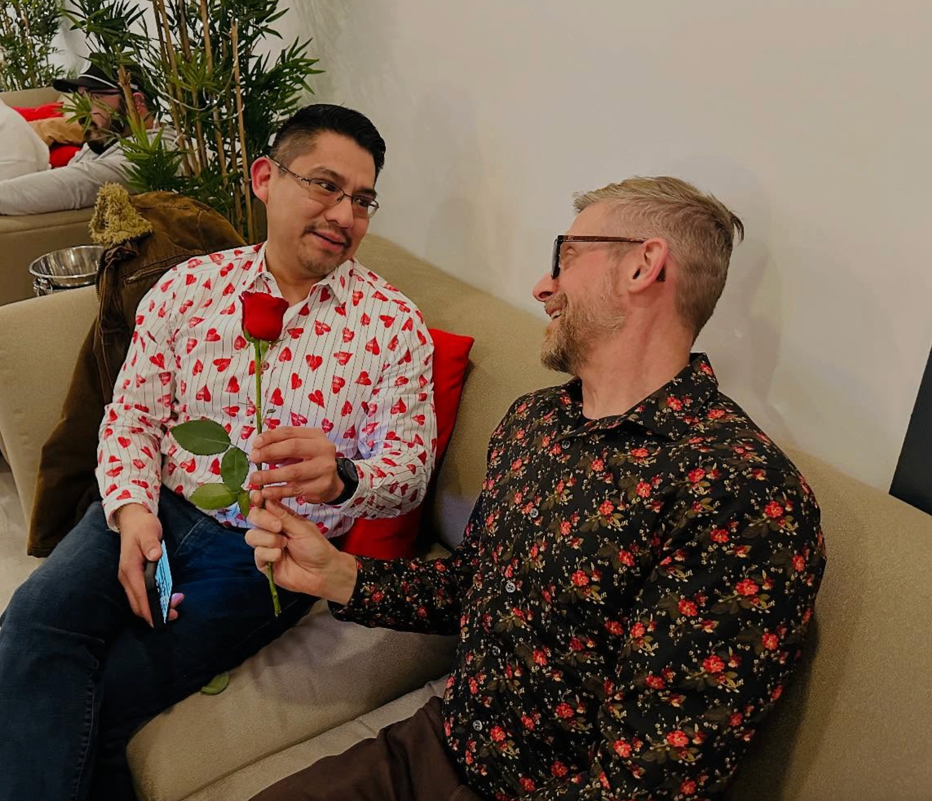Friend in a heart-print shirt handing a red rose to another guest on the lounge