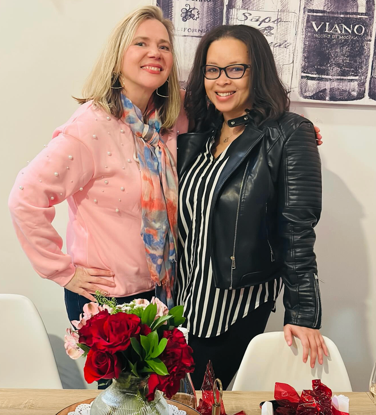 Two friends posing behind a vase of red roses at the Valentine's party